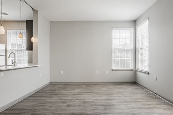 A spacious room with a kitchen area to the left and a large window with blinds on the right wall
